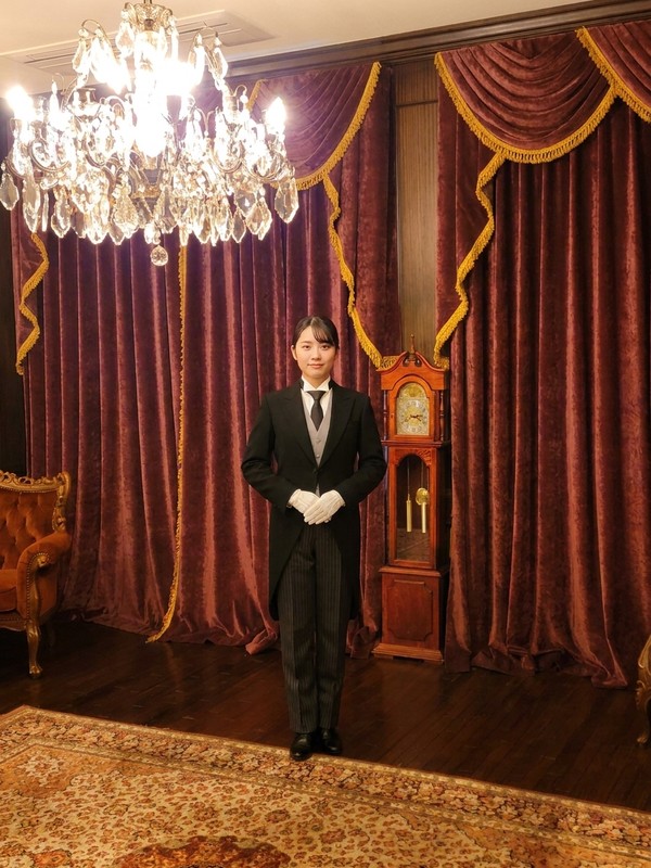 日本執事アカデミー 受講特典・修了証 白手袋と教科書を手にした日本執事アカデミーの正装の女性執事